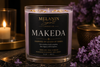 A 10 oz soy wax candle by Melanin Spirit Candle Co. named 'Makeda', in a clear glass jar with a black label and gold glitter accents.